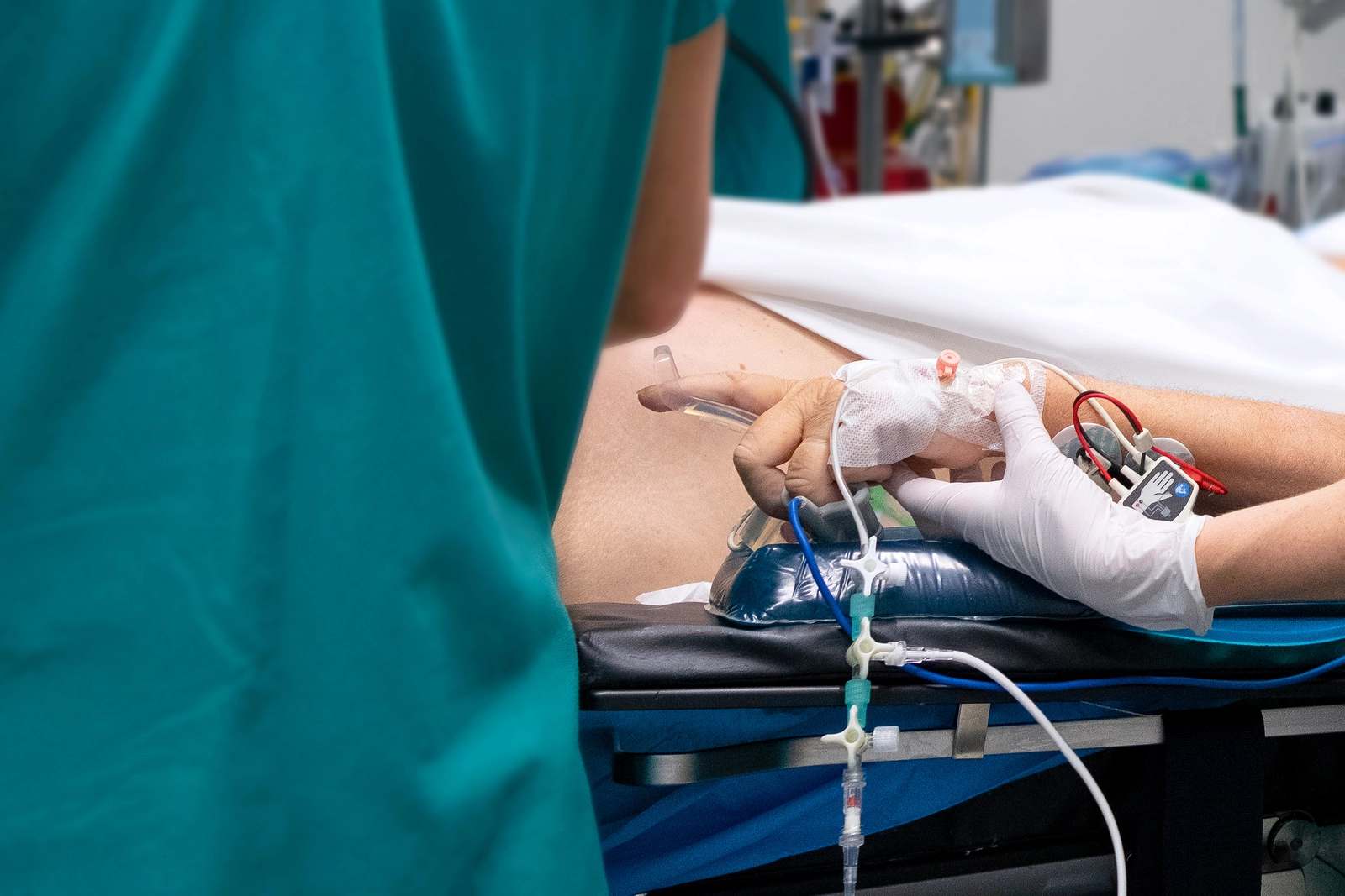 Photo d'une main d'un soignant gantée qui tient la main d'un patient avec des nombreux câbles